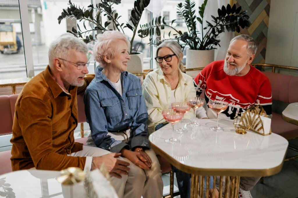 Tres personas mayores sentadas a una mesa, disfrutando de una conversación con copas de vino