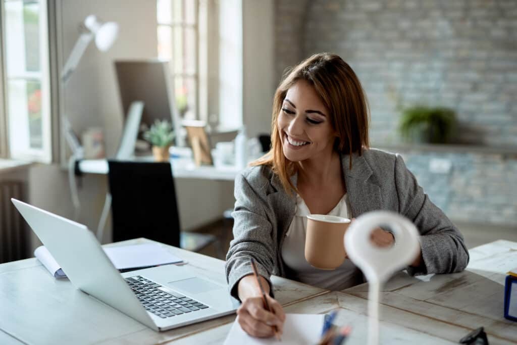 Mujer sonriente sentada a una mesa con un portátil frente a ella.