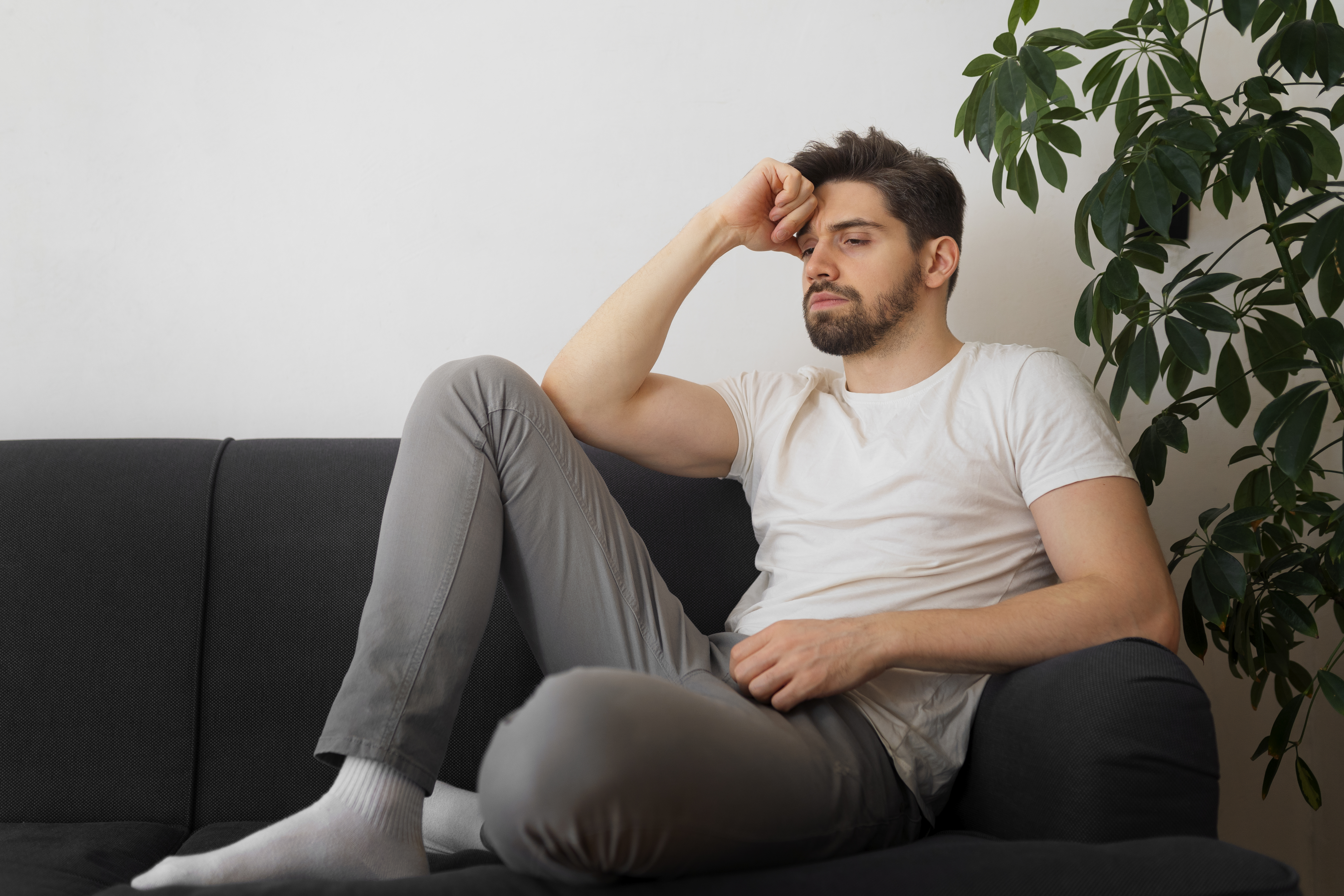 Hombre sentado en el sofá con expresión de preocupación relacionada con estrés, ansiedad o agotamiento emocional.