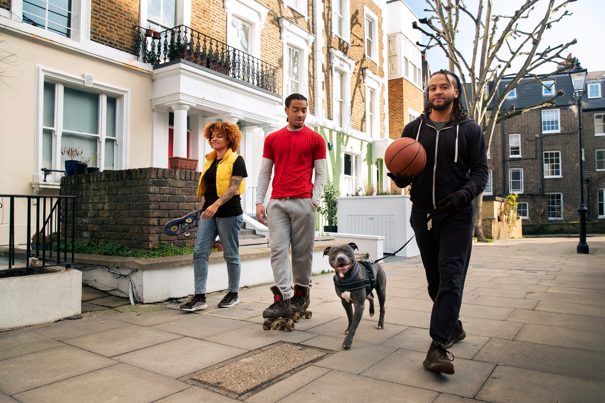 Hombre y mujer paseando un perro, mientras otro hombre lleva un balón de baloncesto